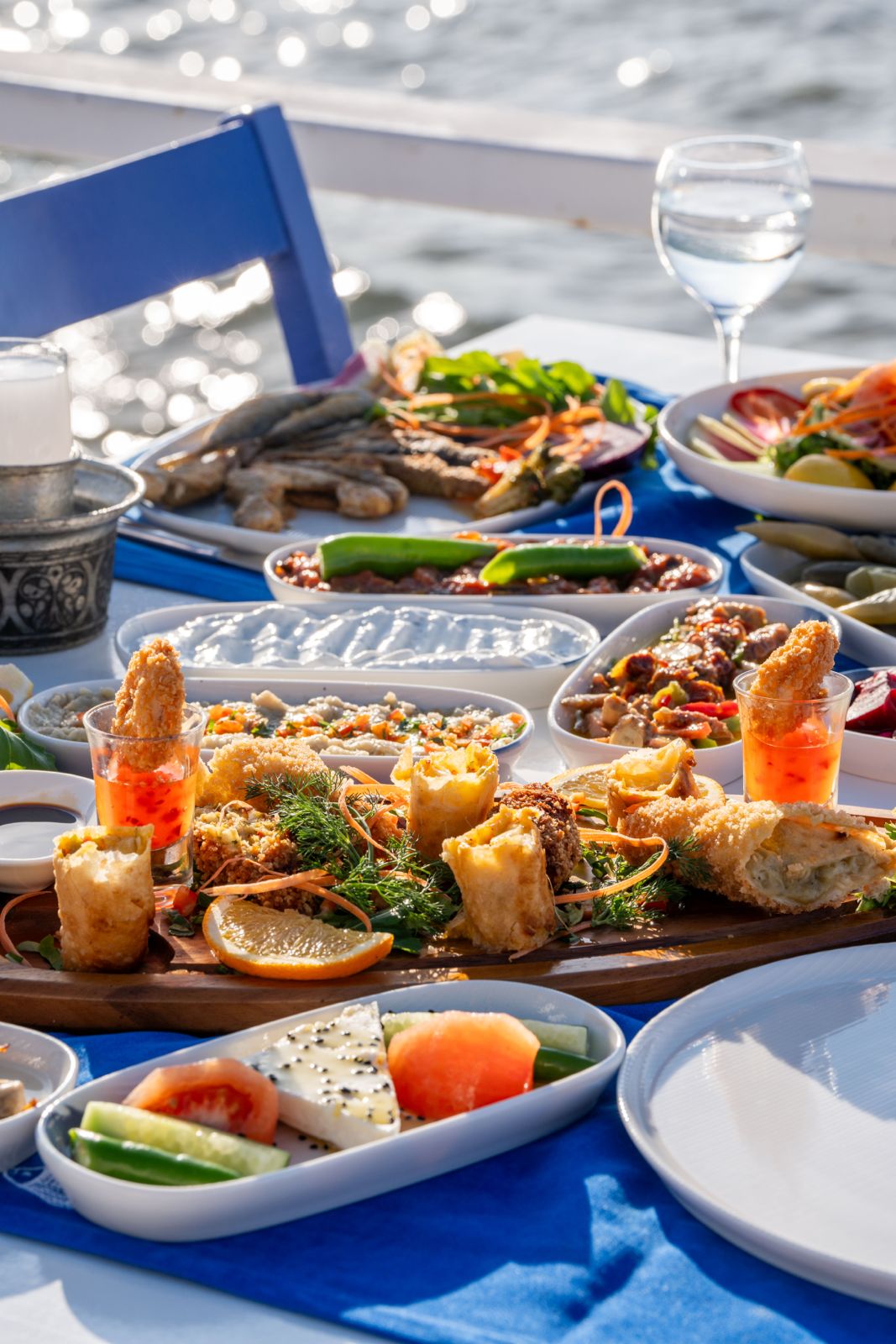 Deniz kenarında güneş ışığında serilmiş zengin meze ve ara sıcak sofrası